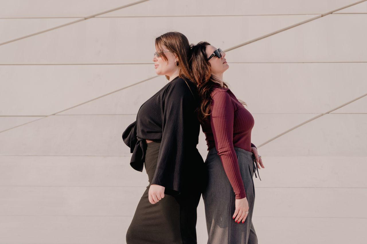 about-us-01 Two fashionable women stand back to back against a modern, minimalist wall. Perfect for lifestyle and fashion themes.